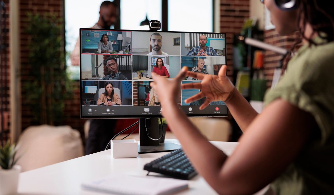 African american startup employee working from home gesturing in video conference with colleagues at desk. Small business owner talking with team in internet call on personal computer with webcam.